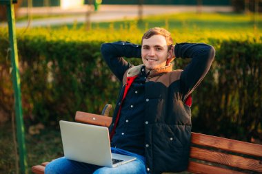 Dizüstü bilgisayar ile bankta oturan genç adam