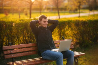 Dizüstü bilgisayar ile bankta oturan genç adam