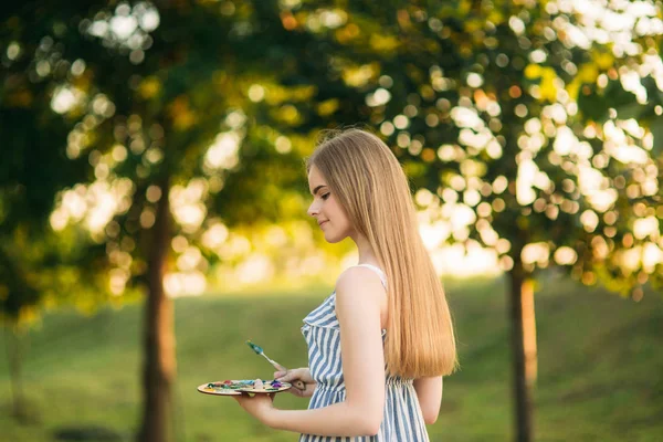 Bella artista ragazza è in piedi nel parco e tenendo tavolozza con vernici — Foto Stock