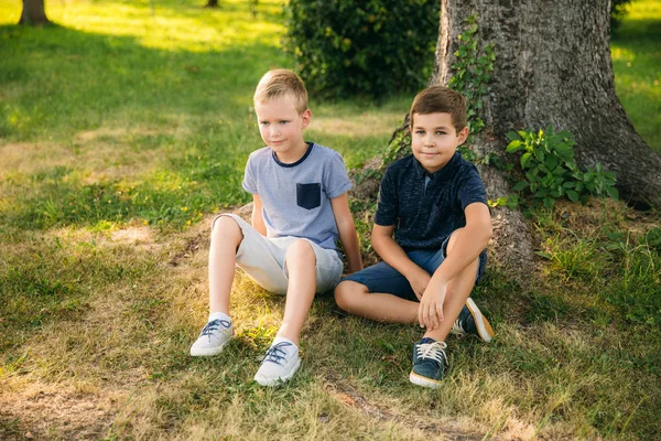 Dos niños juegan en el parque. Dos hermosos chicos en camisetas y pantalones cortos se divierten sonriendo —  Fotos de Stock