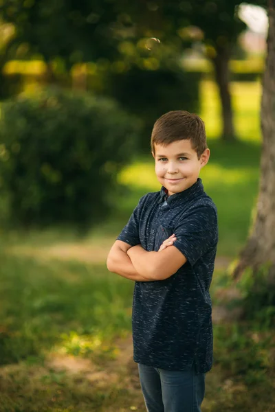 Jóképű fiú mosolyogva, és pózol a fotós. Örömteli gyermek sétál a parkban. Nyári napsütés — Stock Fotó