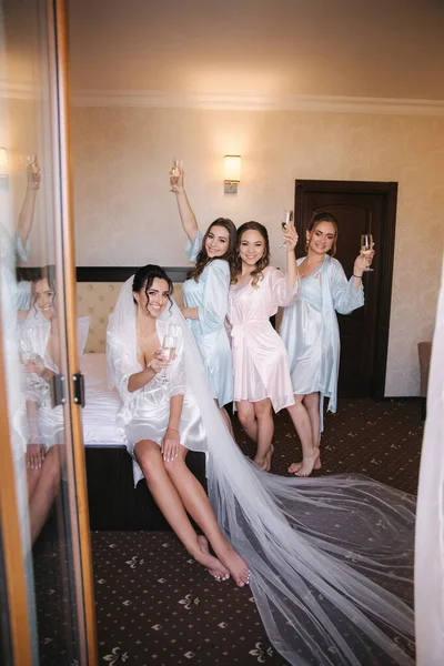 Hermosa novia con las mejores damas de honor bebiendo champán en el hotel. Mañana de novia. Sexy damas de honor en excitante negligee —  Fotos de Stock