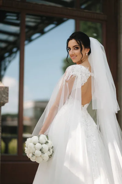 Великолепная невеста в элегантном свадебном платье с букетом белых цветов в день свадьбы — стоковое фото