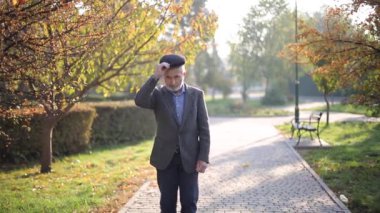 Yakışıklı yaşlı adam gri ceket ve siyah şapka giyiyor. Yaşlı gri saçlı sakallı adam sonbahar parkında yürüyor. Sarı arkaplan