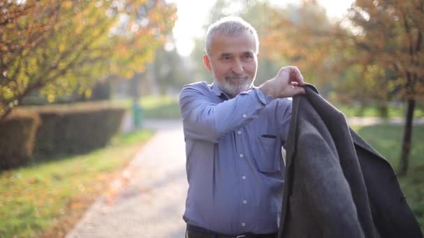 Handsome elderly man putting on a gray jacket. Old gray-haired bearded man walk in the autumn park. Yellow background — Stock Video