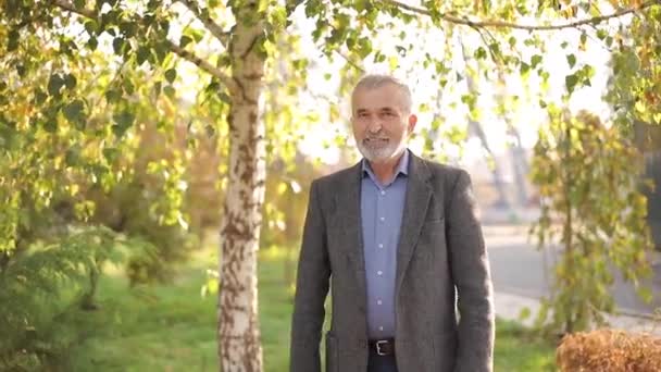 Ritratto di anziano felice nel parco. Uomo barbuto dai capelli grigi in giacca grigia — Video Stock