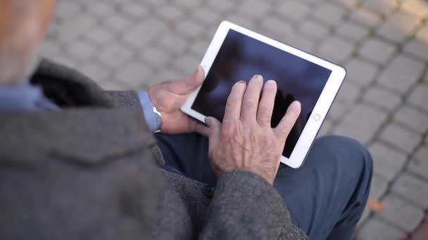 Attrappe eines älteren Mannes mit Tablet draußen. Rückansicht eines älteren Mannes, der auf der Bank sitzt und Tablet benutzt — Stockvideo