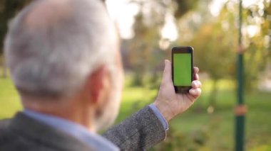 Dışarıda telefon kullanan yaşlı bir adamın maketi. Yeşil ekran. Telefona zarar verecek mesafede bir adamın arka görüntüsü. Dedem akıllı telefondan video çekiyor.