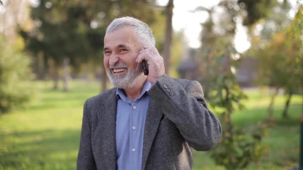 Ευτυχισμένος ηλικιωμένος άντρας μιλάει με κάποιον στο τηλέφωνο. Όμορφος ηλικιωμένος με ωραία γενειάδα χαμογελά και χαίρεται — Αρχείο Βίντεο
