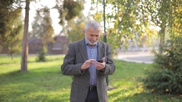 Nahaufnahme eines alten Mannes mit weißem Bart, der sein Smartphone draußen benutzt — Stockvideo