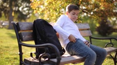 Delikanlı cep telefonundan akıllı telefon çıkardı. Parktaki bankta oturan genç çocuk.