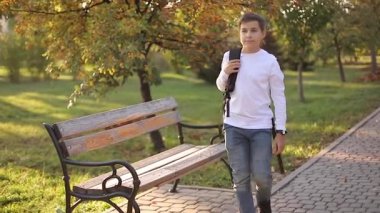 Mutlu okul çocuğu dersten sonra eve döner. Sırt çantalı, beyaz kot pantolonlu bir genç.