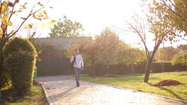 Mutlu okul çocuğu dersten sonra eve döner. Sırt çantalı, beyaz kot pantolonlu bir genç.