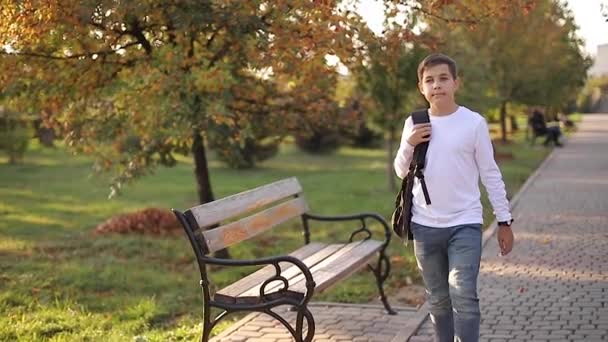 Glad skolpojke går hem efter lektionerna. Tonåring i vit skjorta jeans jeans med ryggsäck — Stockvideo