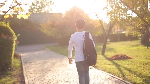 Visão traseira do estudante voltar para casa depois das aulas. Adolescente de camisa branca jeans jeans jeans com mochila — Vídeo de Stock