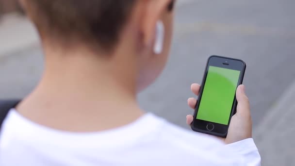 Scherzo di ragazzo adolescente con cuffie wireless utilizzare il telefono otside. Schermo verde — Video Stock