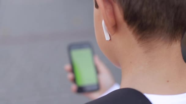 Scherzo di ragazzo adolescente con cuffie wireless utilizzare il telefono otside. Schermo verde — Video Stock