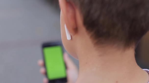 Mock up των εφήβων αγόρι με ασύρματα ακουστικά χρησιμοποιούν το τηλέφωνο otside. Πράσινη οθόνη — Αρχείο Βίντεο
