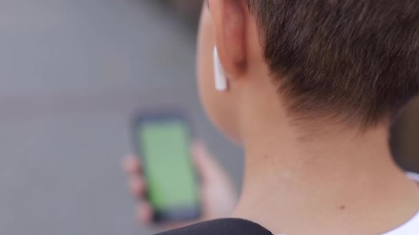 Mock up of teenage boy with wireless headphones use phone otside. Green screen — Stock Video