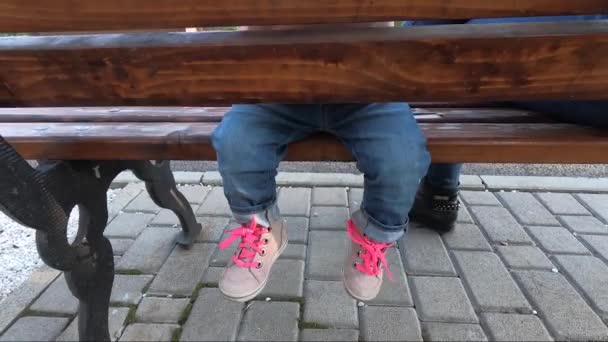 小さな女の子は公園で食べると、お母さんは赤ちゃんの果物を与える。母と娘がベンチに座って — ストック動画