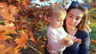 Anne küçük kızıyla kırmızı ağacın önünde duruyor. Sonbahar Parkı