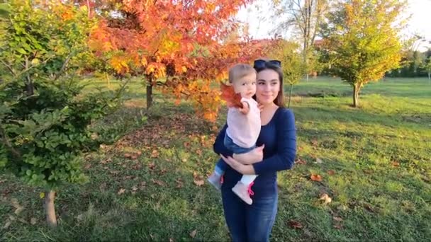 A mãe com a filhinha fica em frente à árvore vermelha. Parque de outono — Vídeo de Stock