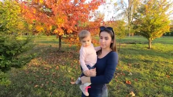 Madre con su pequeña niña de pie frente al árbol rojo. Parque de otoño — Vídeos de Stock