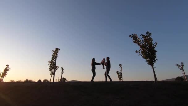 Silueta de mamá papá y su hija caminando en el parque a través del adorno. Familia feliz pasar tiempo juntos — Vídeo de stock