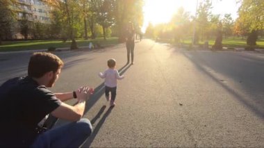 Sevimli küçük kız anne ve babasıyla parkta yürümek için çalışıyor. On aylık tatlı bebek yürüyüşü. Güzel, mutlu bir kız. Sonbahar havası