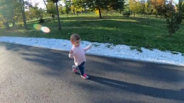 Sevimli küçük kız ekim ayında parkta yürüyor. On aylık tatlı bebek yürüyüşü. Güzel, mutlu bir kız. Sonbahar havası