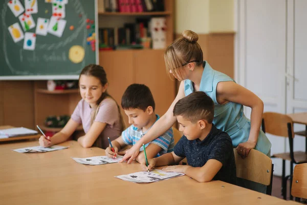 Учитель помогает школьникам писать тесты в классе. образование, школа, обучение и человеческая концепция — стоковое фото