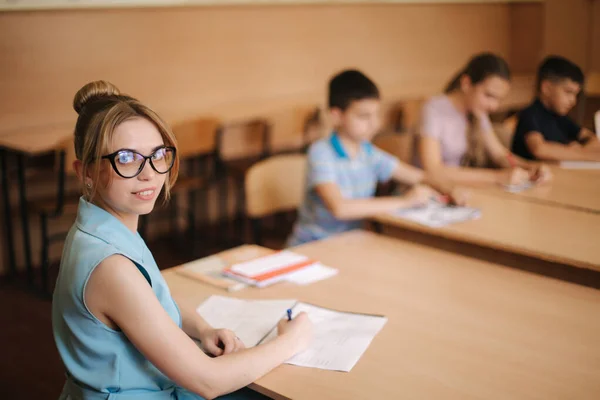 Bonita maestra en el aula sentada en el escritorio y preguntando a los niños. educación, escuela primaria, aprendizaje y concepto de personas — Foto de Stock