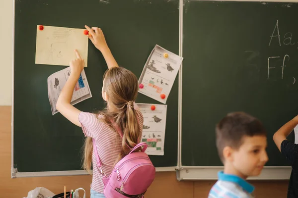 Schoolgirl writing something on blackboard in classroom — Stock Photo, Image