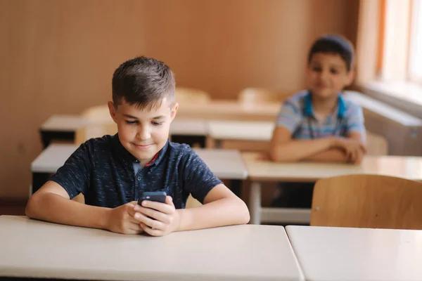 Roztomilý chlapeček používá telefon během lekce. Dva schollpáni ve třídě — Stock fotografie