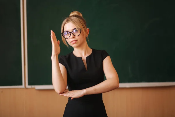 Νεαρή δασκάλα με γυαλιά στέκεται μπροστά στον μαυροπίνακα — Φωτογραφία Αρχείου