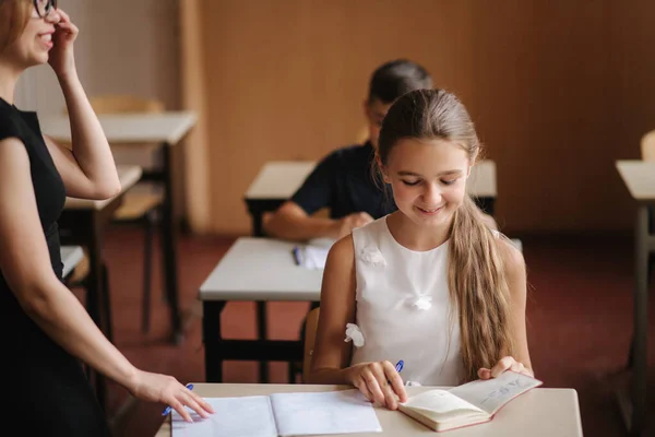 Lärare hjälper skolbarn att skriva prov i klassrummet. utbildning, grundskola, lärande och människor koncept — Stockfoto