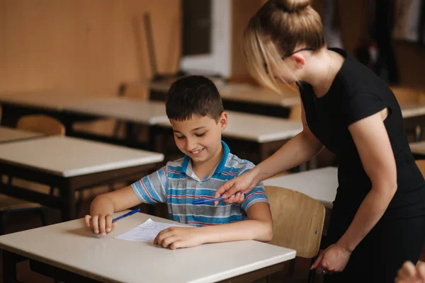 Lehrer hilft Schülern beim Schreiben von Tests im Klassenzimmer. Bildung, Grundschule, Lernen und Menschen-Konzept — Stockfoto