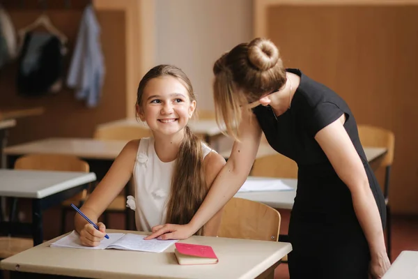 Profesor ayudando a los niños de la escuela a escribir prueba en clase. educación, escuela primaria, aprendizaje y concepto de personas — Foto de Stock