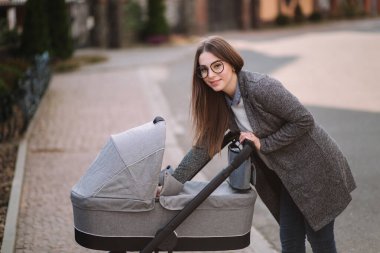 Genç Anne yürümek ile kız içinde Stroller. Annem bebeği önemsiyor. Anne Puset için bakmak ve bebek uyku yardım
