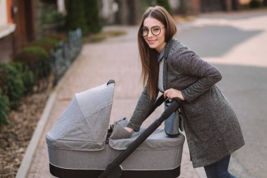 Genç Anne yürümek ile kız içinde Stroller. Annem bebeği önemsiyor. Anne Puset için bakmak ve bebek uyku yardım