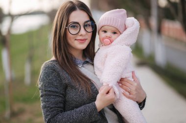 Anne ve küçük kızının portresi. Güzel bir anne ve sevimli bir bebek. Anne Hud kızı. Fıstık rengi şapka ve meme ucu oyuncağı giymiş bebek. Anne kızını öp.