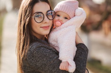 Anne ve küçük kızının portresi. Güzel bir anne ve sevimli bir bebek. Anne Hud kızı. Fıstık rengi şapka ve meme ucu oyuncağı giymiş bebek. Anne kızını öp.