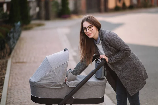 Young mom walking with daughter in stroller. Mother cares for the baby. Mom look in to the stroller and help baby to sleep