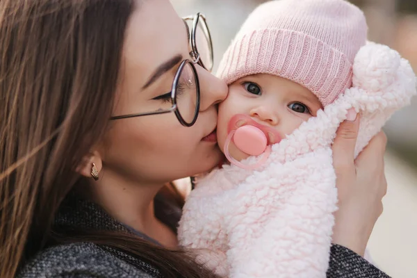 Ritratto di madre e della sua bambina. Bella mamma e bambino carino. La madre abbraccia sua figlia. Bambino vestito con cappello color arachide e capezzolo giocattolo. Mamma bacio sua figlia — Foto Stock