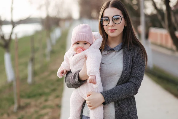 Little Baby Girl na ręce matek w różowe ubrania. Cute baby z orzech kolor brodawki zabawka — Zdjęcie stockowe
