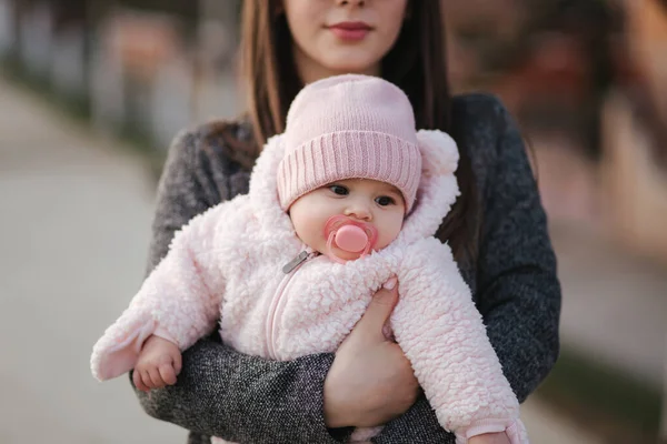 Kleine baby meisje op moeders handen in roze kleren. Schattige baby met peanch kleur tepel speelgoed — Stockfoto