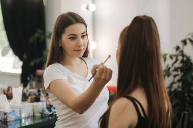 Güzellik stüdyosu modeli ile makyaj sanatçısı çalışma. Şık Kızıl saçlı model için moda yapmak