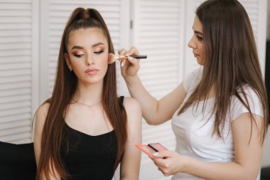 Kadın makyaj ustası bir toz fırça kullanın. Güzellik stüdyosunda güzel bir model. Profesyonel makyaj sanatçı bitirmek moda maleup. Beyaz katlanır ekranın arka planı