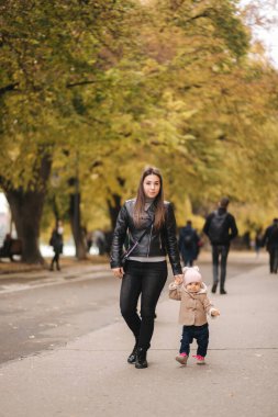 Anne kızıyla birlikte parkta yürüyor. Küçük mutlu kız dışarıda annesiyle yürüyor.