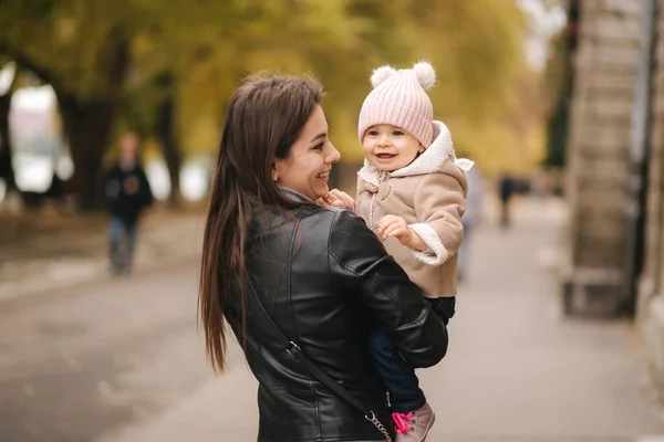 Imádnivaló kislány az anyák kezén a parkban. Anya kisétál a lányával. Boldog család az arany ősszel — Stock Fotó